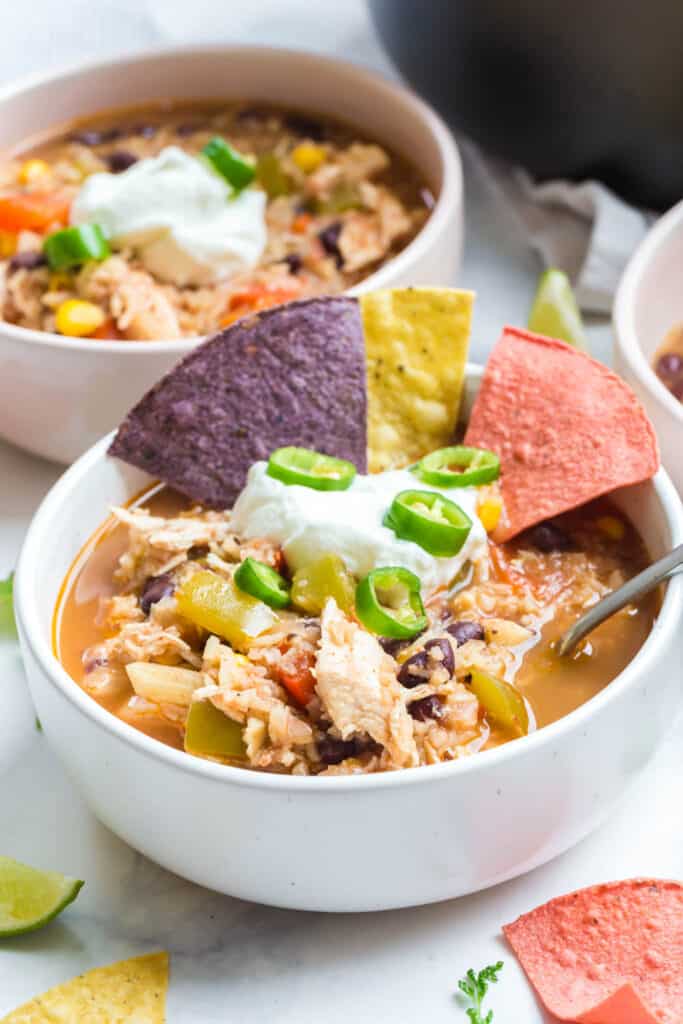 a bowl of this instant pot southwest chicken soup served with plain Greek yogurt, tortilla chips, and sliced jalapeños with more bowls of soup in the background