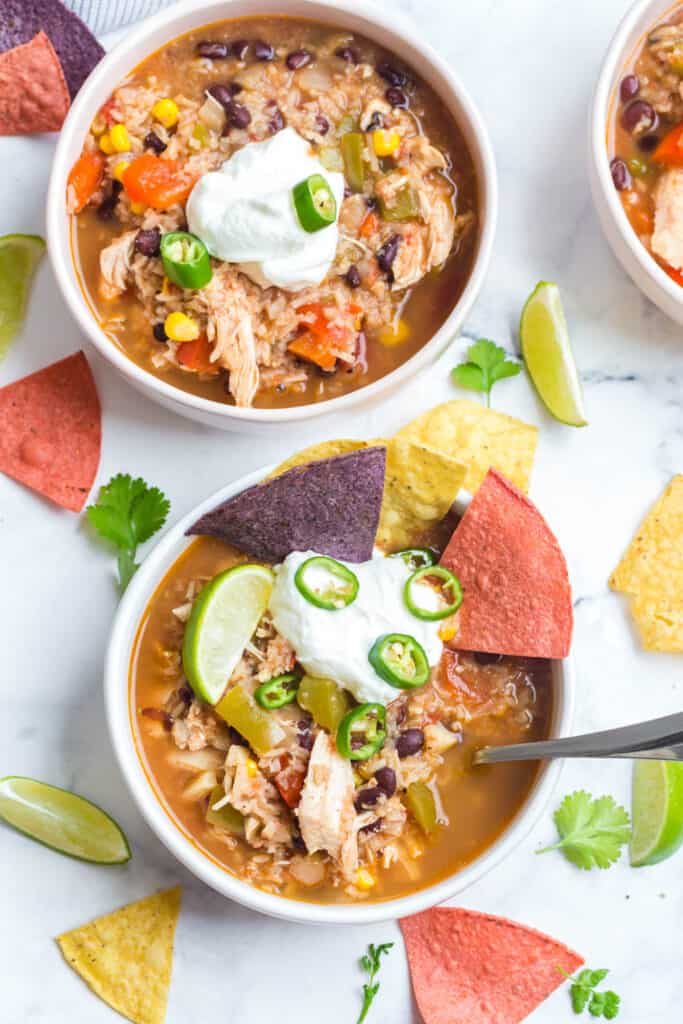 an overhead shot of a bowl of this instant pot southwest chicken soup served with plain Greek yogurt, tortilla chips, and sliced jalapeños with more bowls of soup in the background