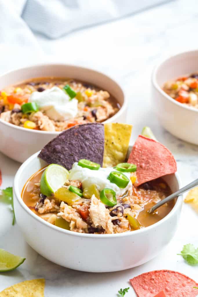 a bowl of this instant pot southwest chicken soup served with plain Greek yogurt, tortilla chips, and sliced jalapeños with more bowls of soup in the background