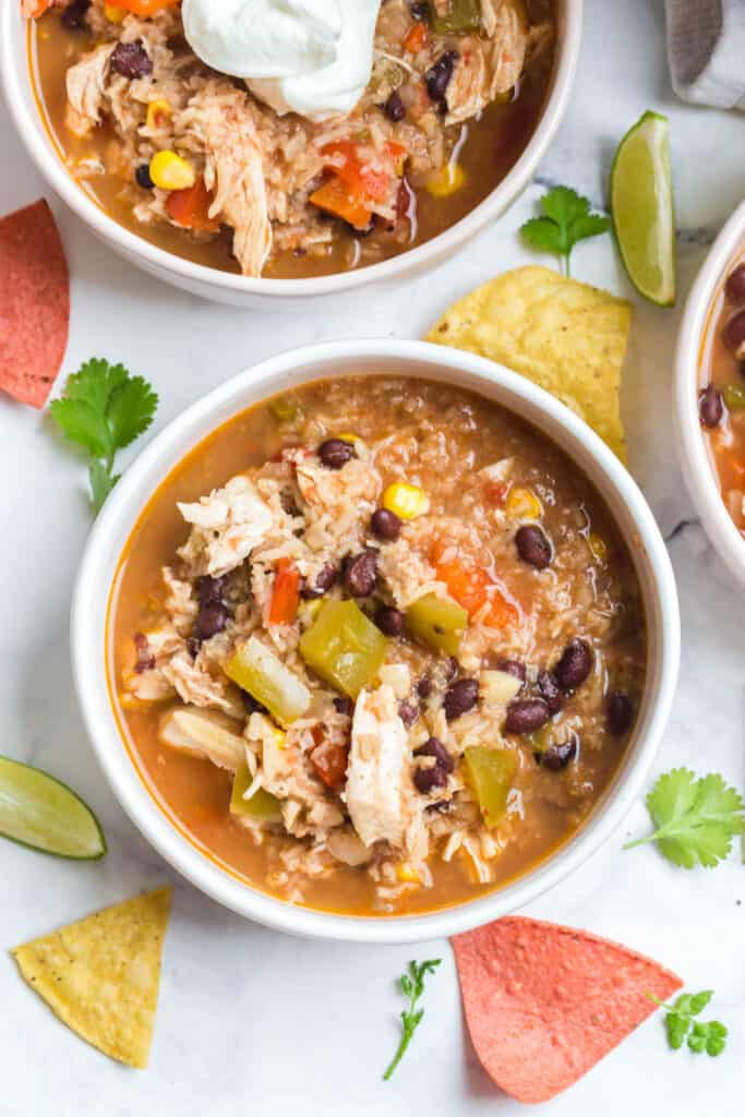 an overhead shot of a bowl of this instant pot southwest chicken soup served with plain Greek yogurt, tortilla chips, and sliced jalapeños with more bowls of soup in the background