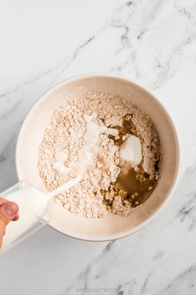 pouring milk and into a bowl of oats and gluten free flour for cookies