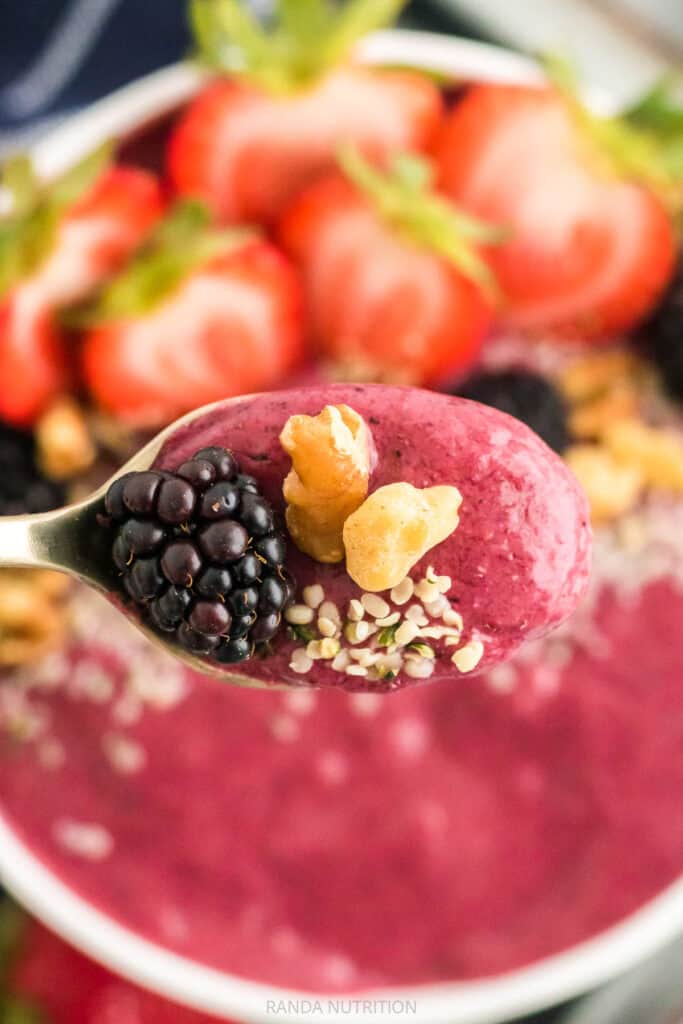 close up of spoon with bee pollen, nuts, black berries from a smoothie bowl