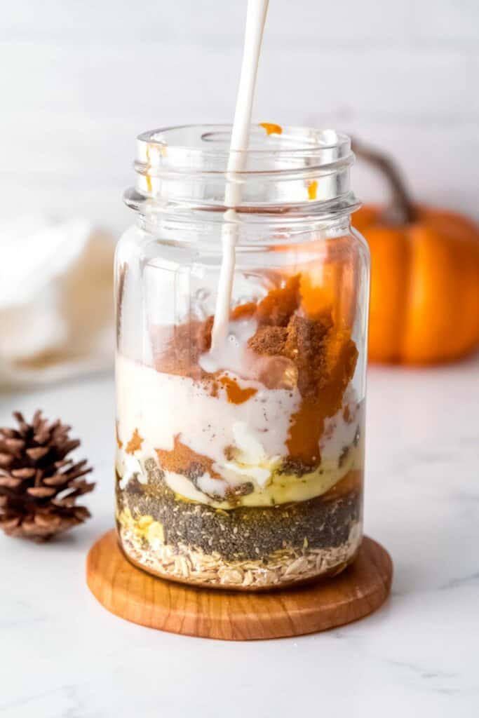 pouring milk into a mason jar with canned pumpkin, chia seeds, oats, and maple syrup