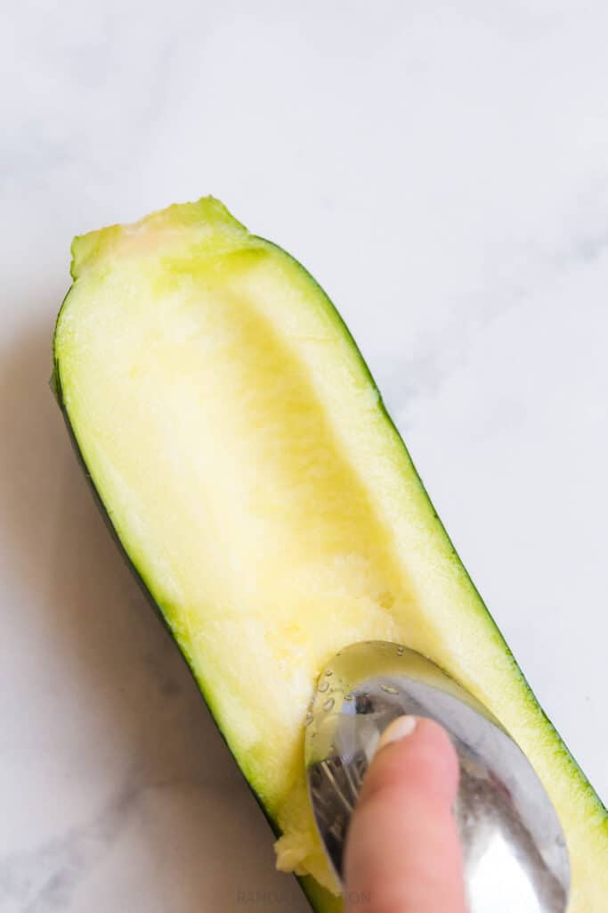 using a spoon to scoop the insides out of a zucchini