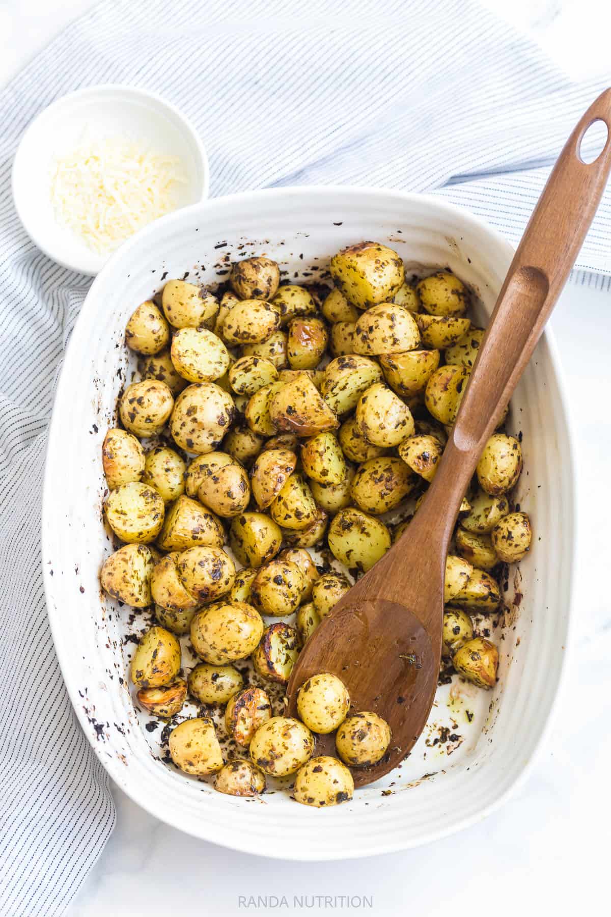 2 ingredient pesto potatoes in a white casserole dish with parmesan on the side