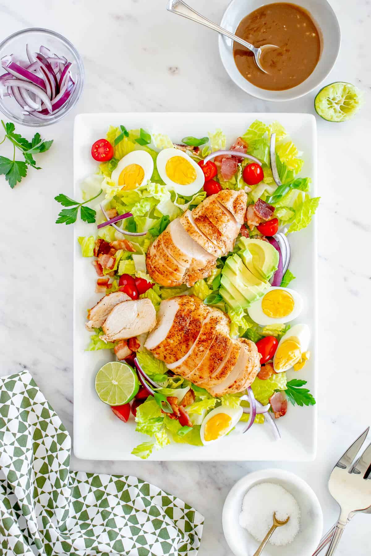 overhead shot of a salad on a platter. Romaine lettuce, tomatoes, eggs, grilled chicken, bacon
