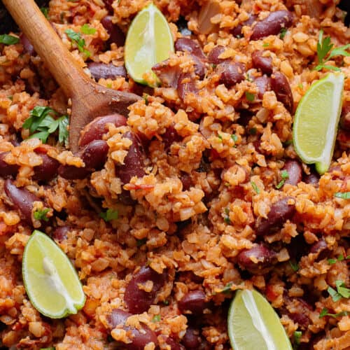 healthy Mexican cauliflower rice recipe being served from a skillet with a wooden spoon.