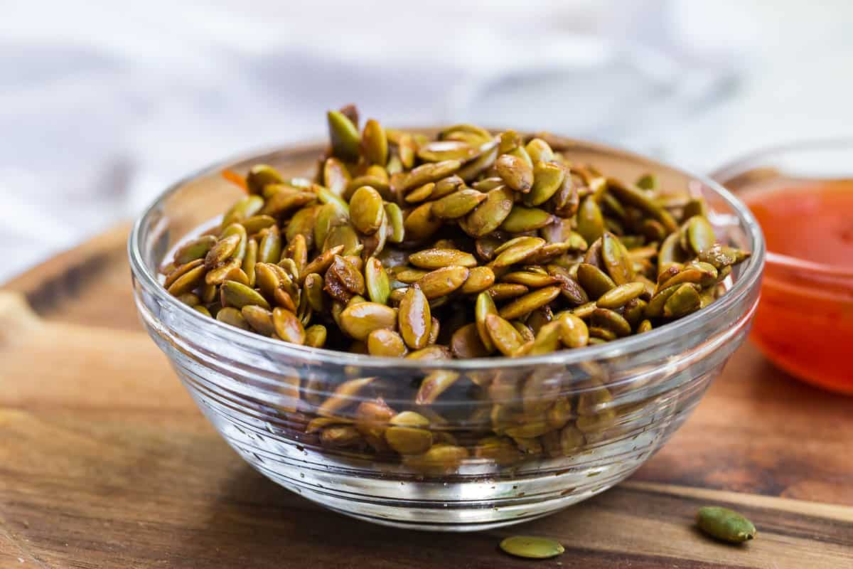 a clear bowl with pumpkin seeds and sweet thai chili sauce