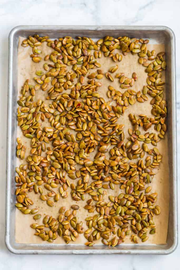 mixing pumpkin seeds on a baking sheet to roast