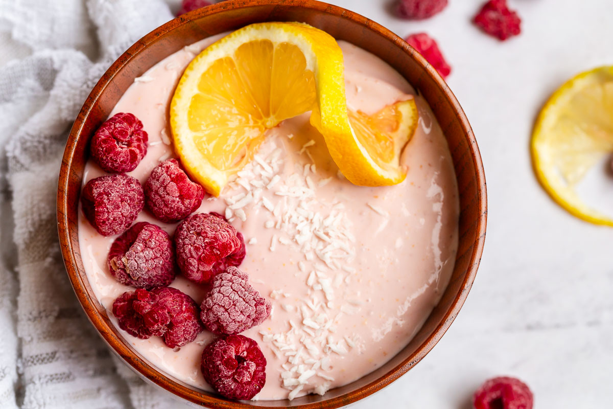 close up shot of cottage cheese blended with raspberries in a wooden bowl topped with lemons and raspberries