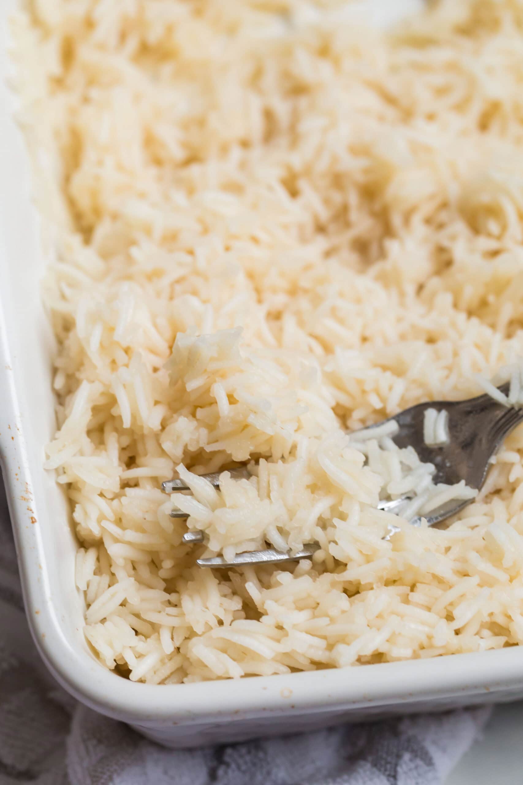 How to Cook Rice In The Oven (White, Brown, or Converted Rice) 3 Cooked rice in the oven being fluffed with a fork.