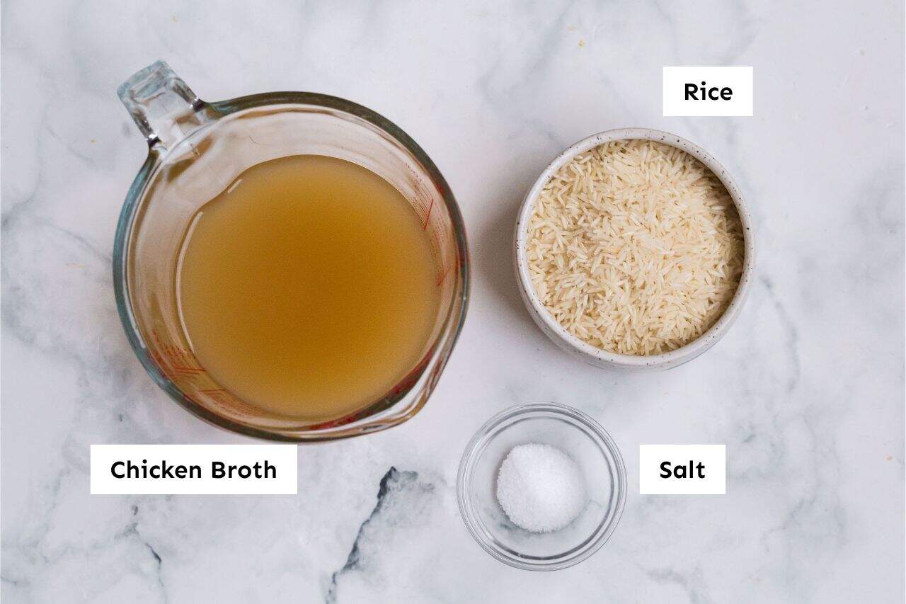 How to Cook Rice In The Oven (White, Brown, or Converted Rice) 2 chicken broth, rice, and salt on a marble background