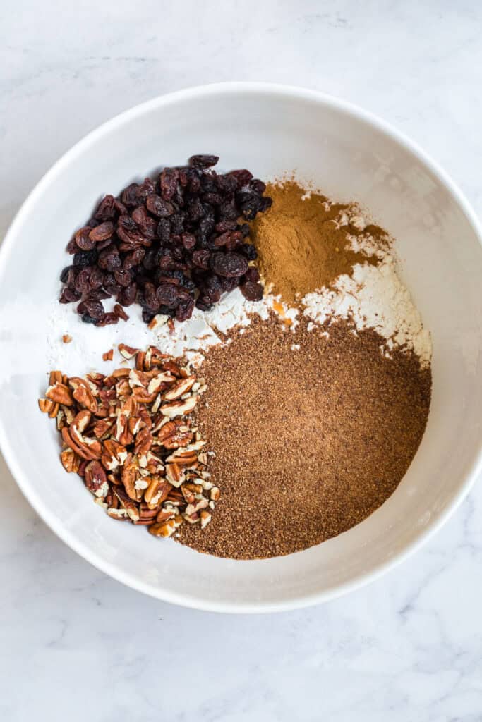 Gluten Free Morning Glory Muffins (Healthy & Moist) 3 Dry ingredients for gluten free morning glory muffins including gluten-free flour, cinnamon, baking soda, raisins, and chopped pecans.