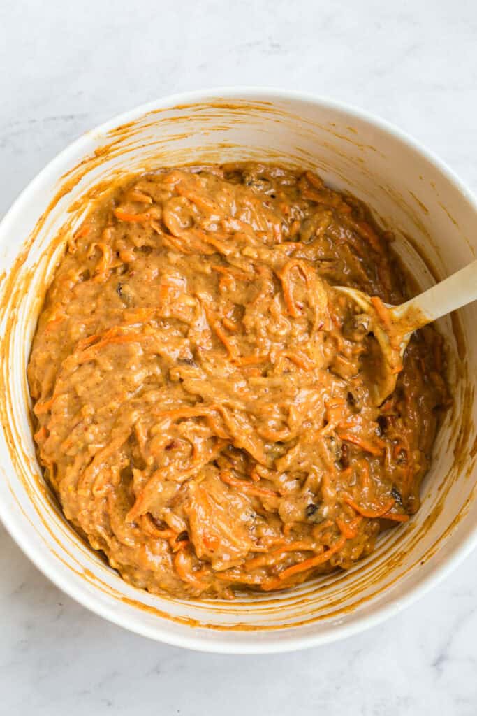 Gluten Free Morning Glory Muffins (Healthy & Moist) 5 Gluten free morning glory muffin batter mixed with shredded carrots, apple, raisins, and spices in a white bowl.