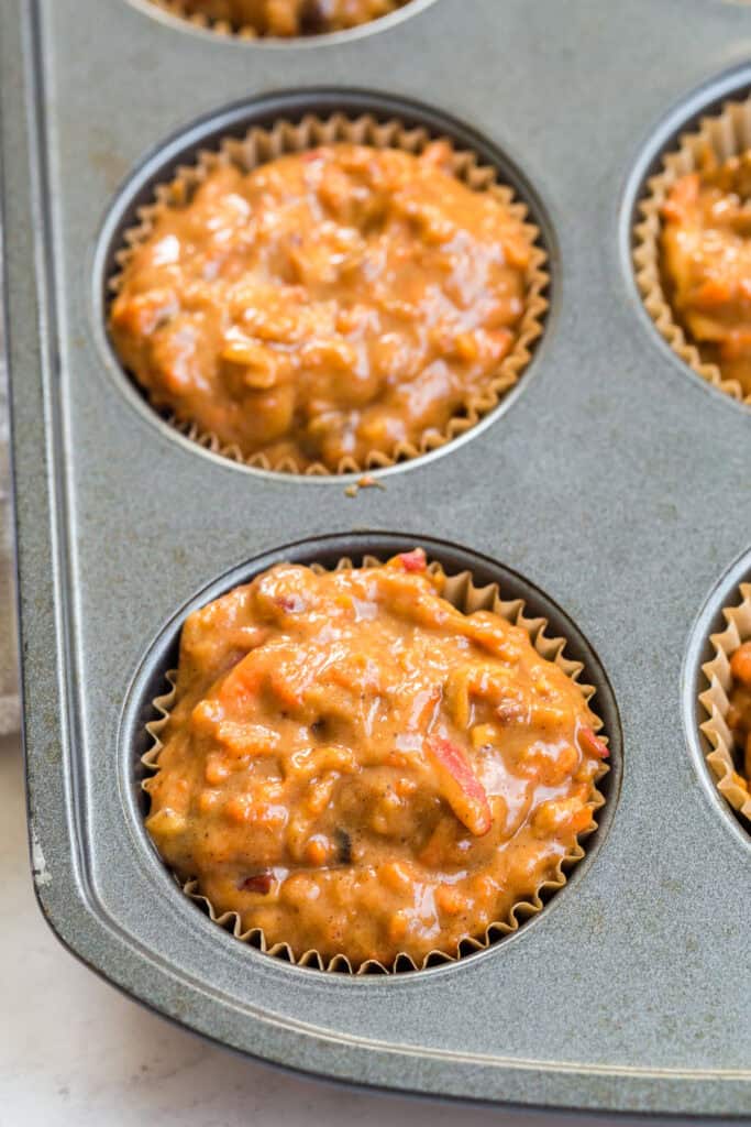 Gluten Free Morning Glory Muffins (Healthy & Moist) 6 Gluten free morning glory muffin batter scooped into a lined muffin tin before baking.