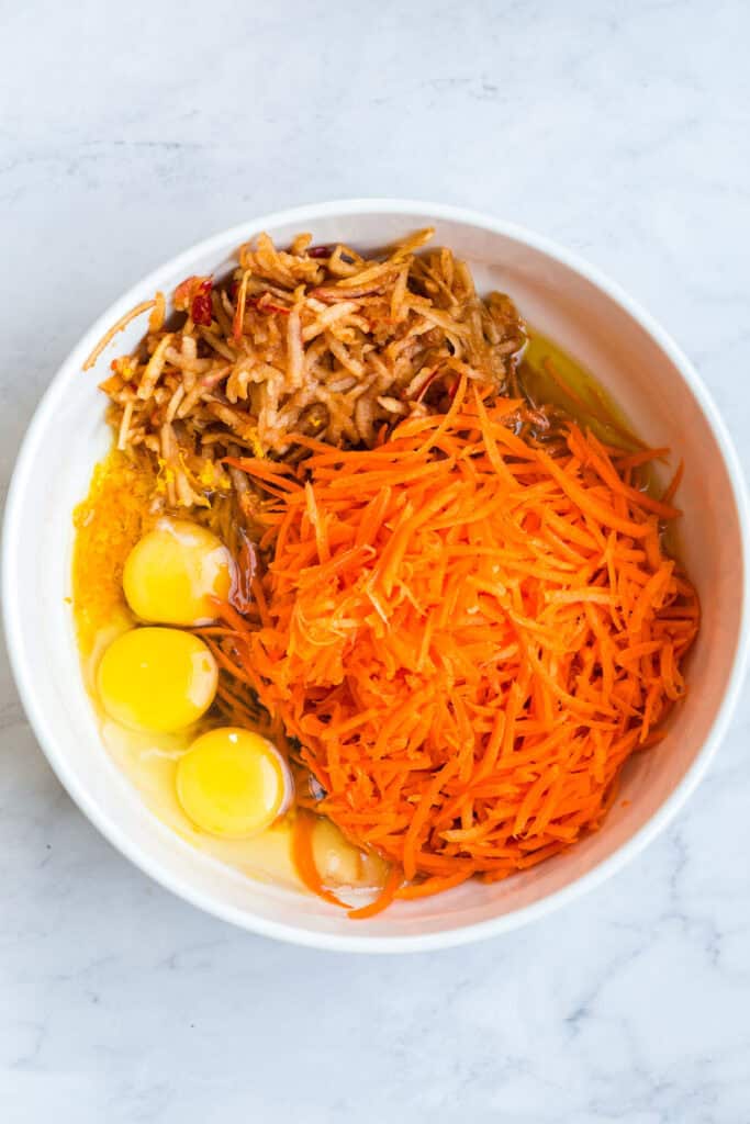 Gluten Free Morning Glory Muffins (Healthy & Moist) 4 Wet ingredients for gluten free morning glory muffins including eggs, shredded carrots, grated apple, oil, and orange zest in a bowl.