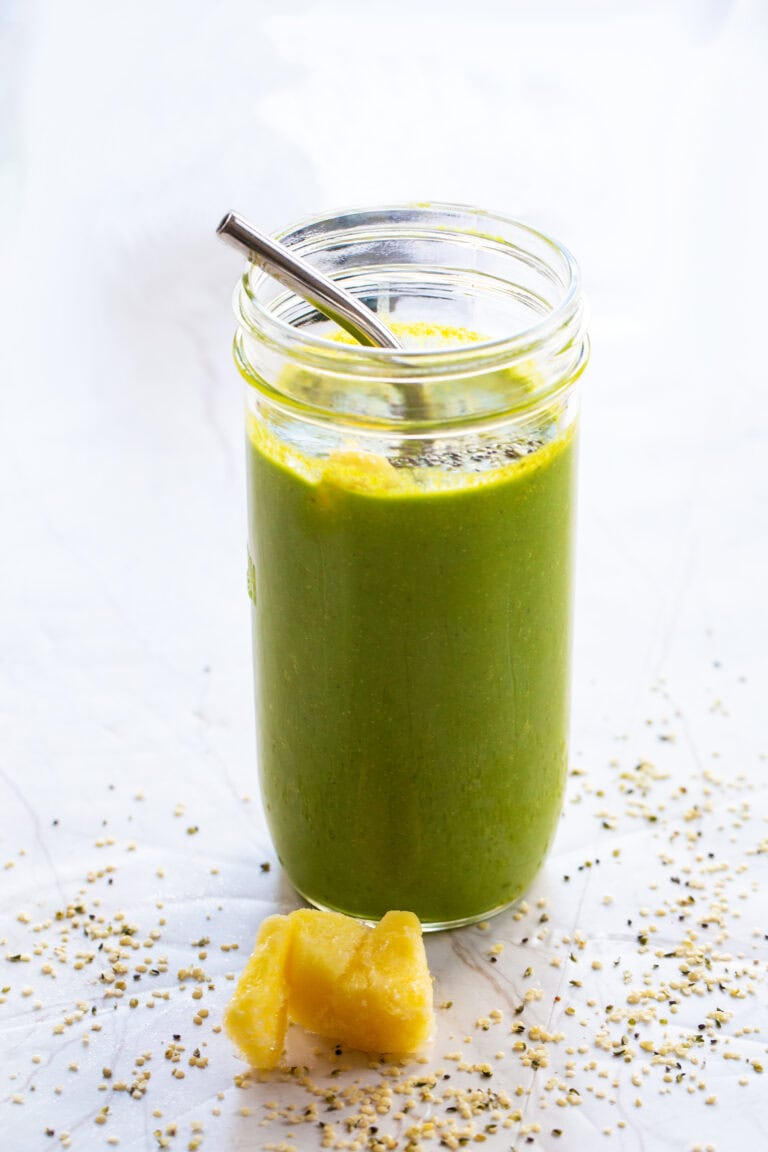 Anti-Inflammatory Green Smoothie 4 Anti-inflammatory green smoothie in a tall glass jar with a metal straw, frozen pineapple and hemp hearts on the counter